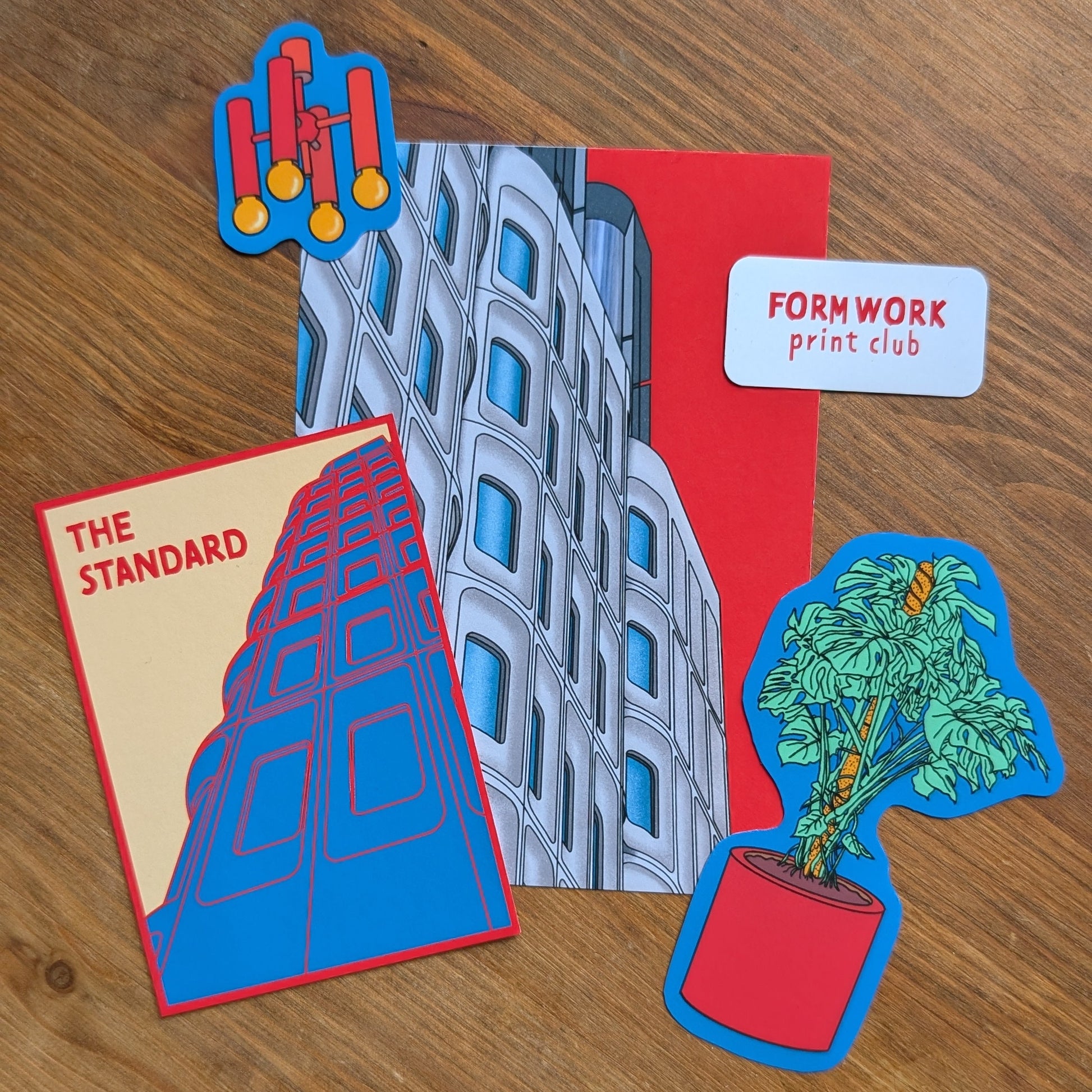 Four colorful stickers on a wooden surface, including 'The Standard' and 'Formwork Print Club'.